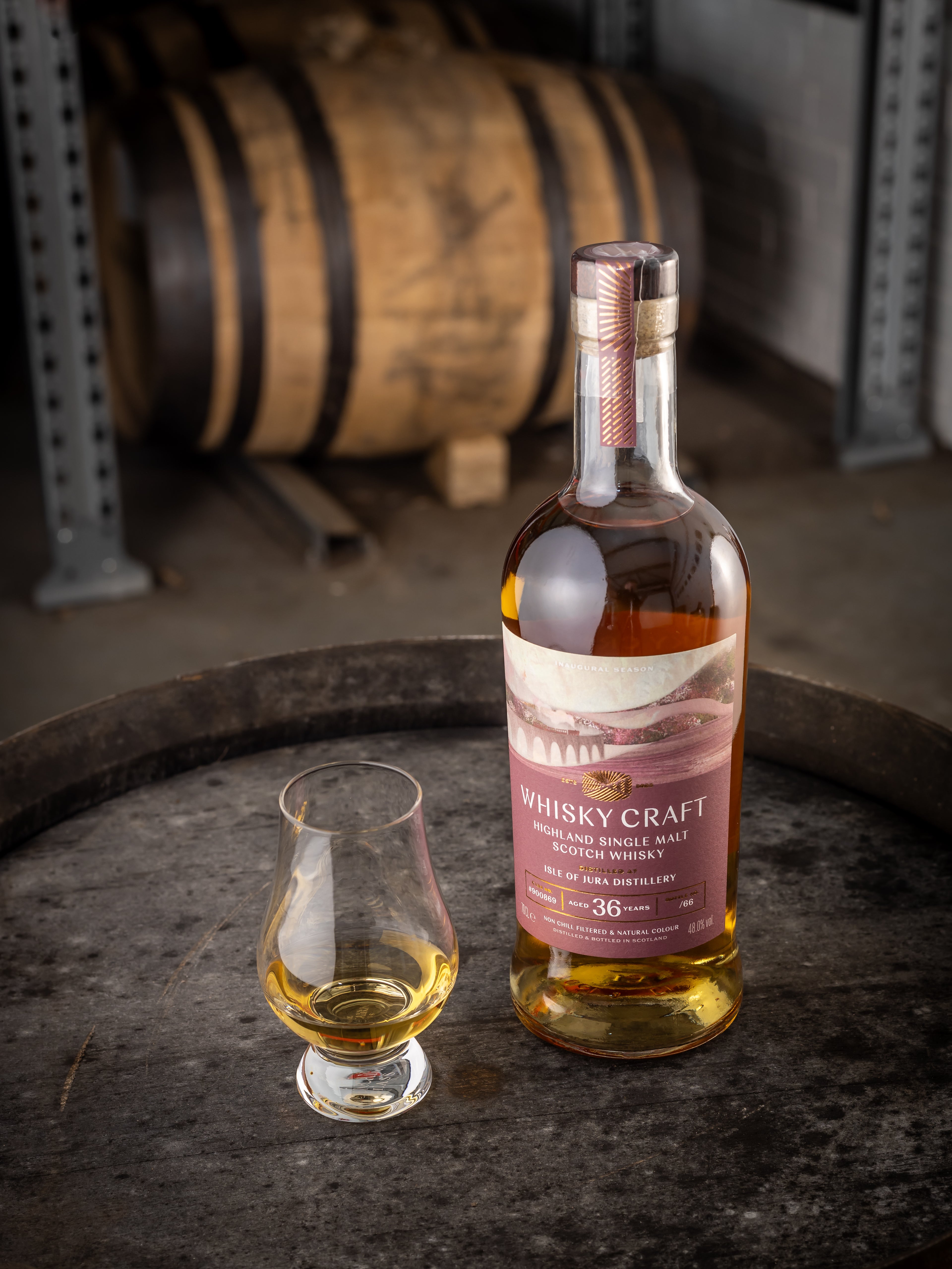 Bottle of Jura whisky with a dram sitting on the top of a barrel, with another in the background