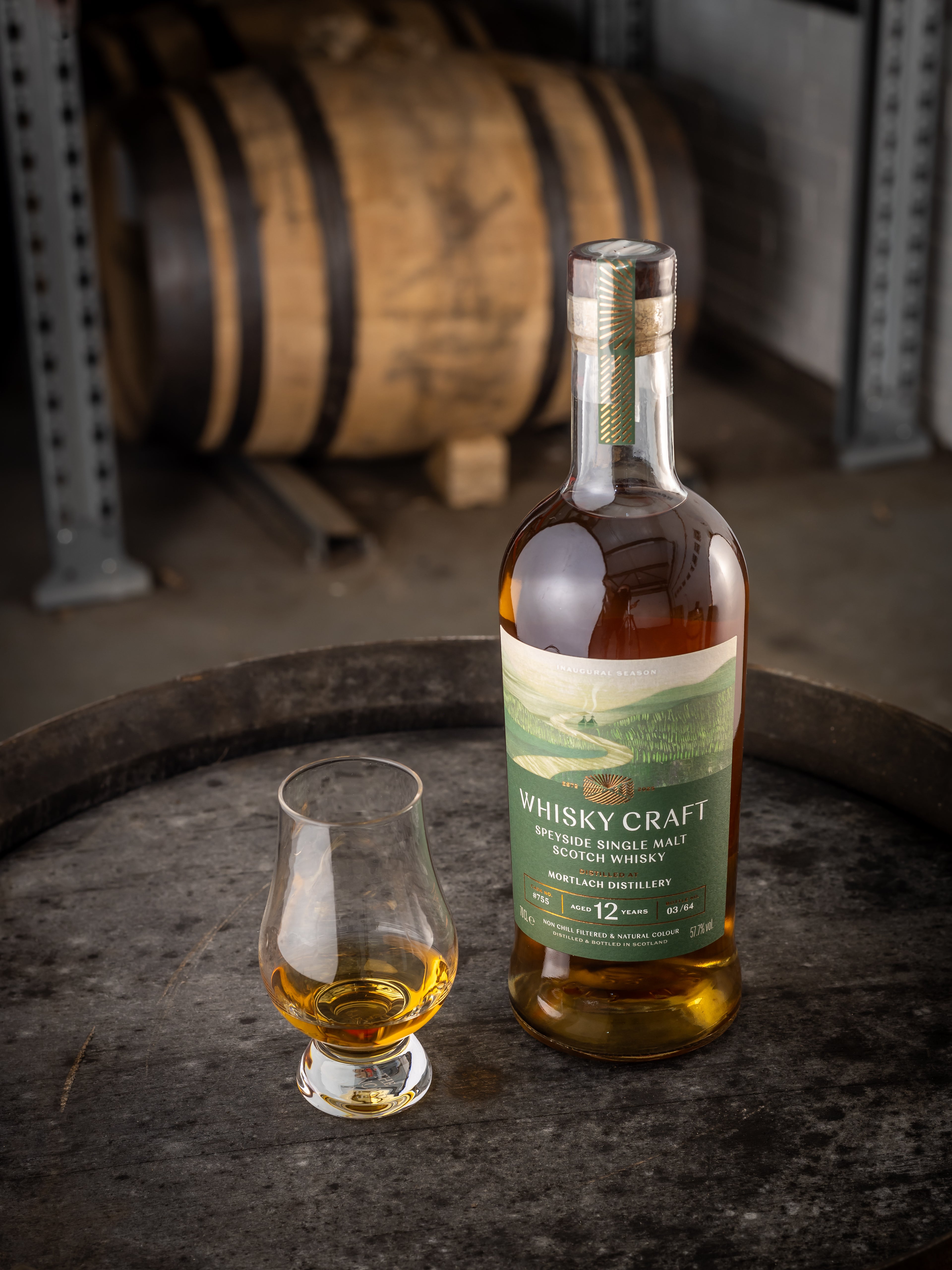 Bottle of Mortlach whisky with a dram sitting on the top of a barrel, with another in the background
