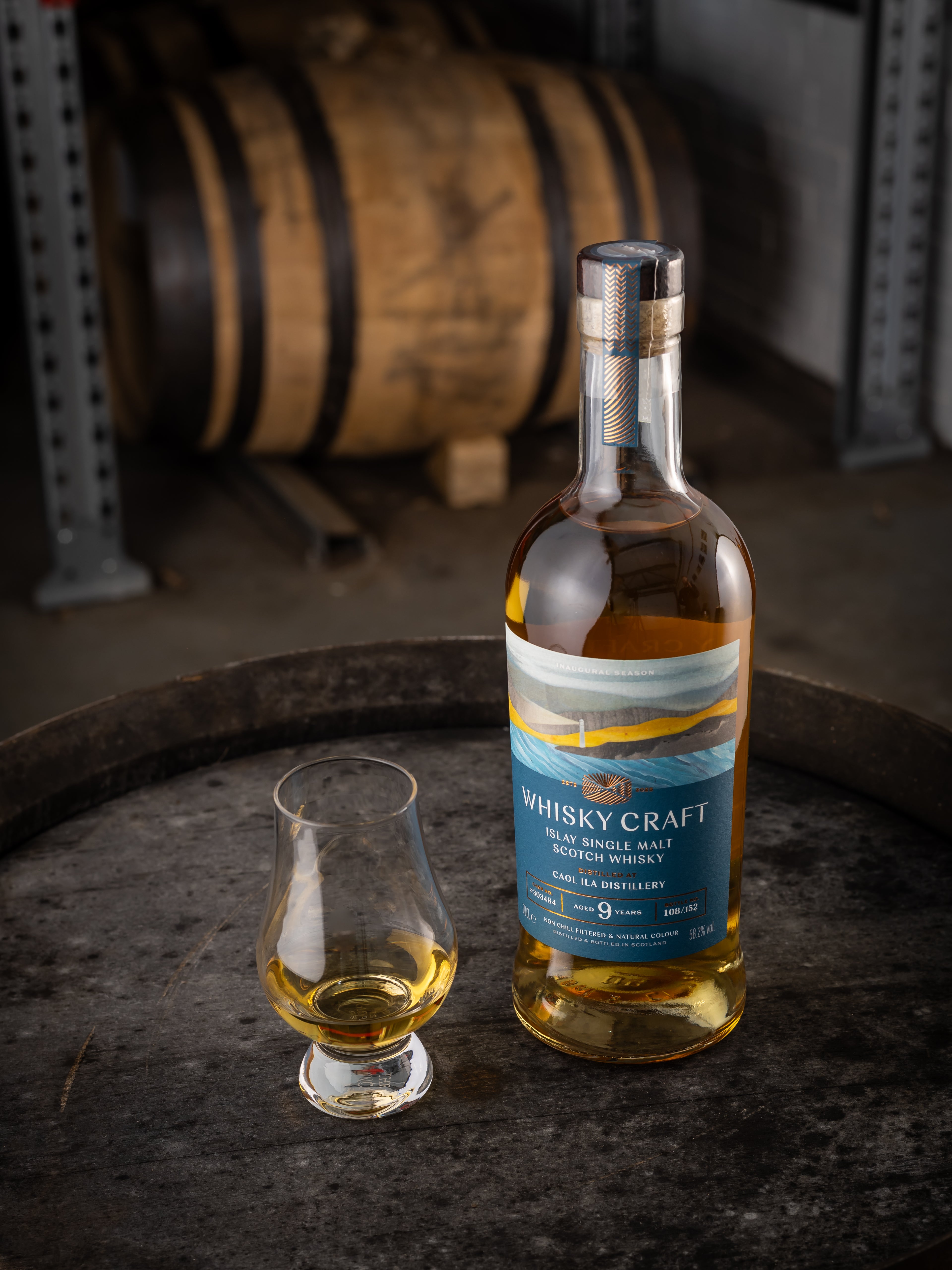 Bottle of Islay whisky with a dram sitting on the top of a barrel, with another in the background
