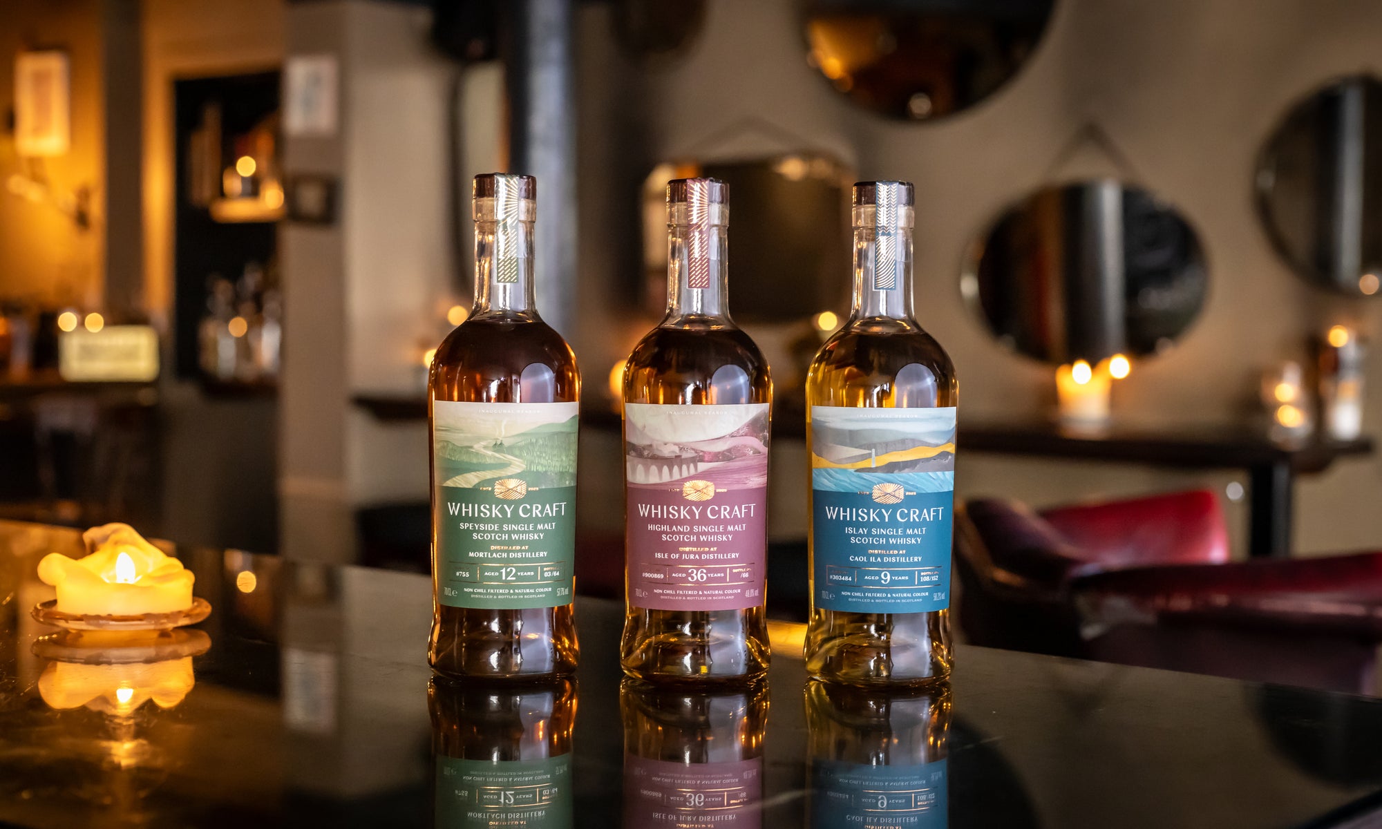 Three bottles of whisky on a wooden table in front of a very decorated room with candles and mirrors