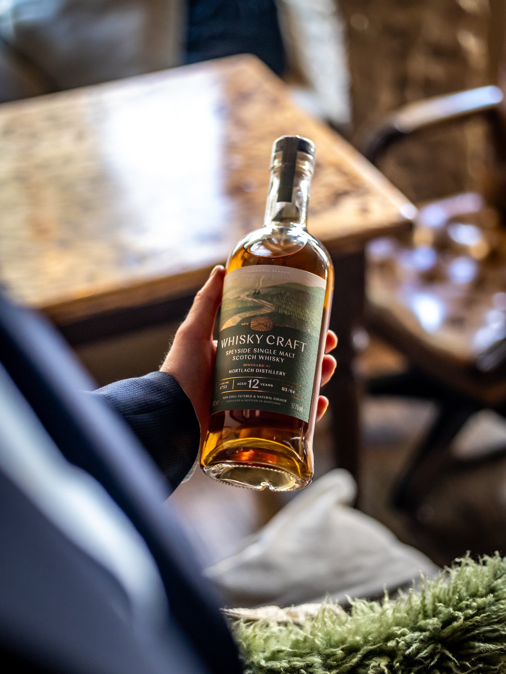 Looking down from someone's shoulder at them holding a bottle of Mortlach whisky in their opposite hand, in a refined drawing room